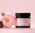 Skincare jar with pink floral design, next to a pink rose and dark textured stone on a pink background.